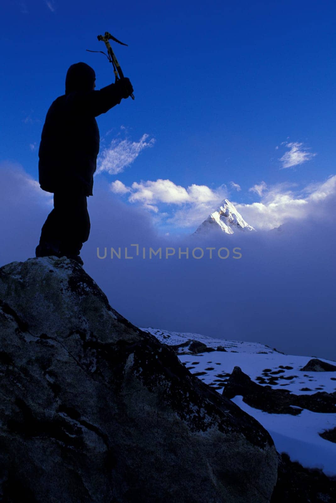 Mountaineer on peak with mountain peak rising out of clouds in background