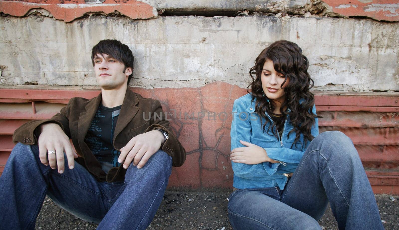 Young trendy couple sitting on the sidewalk