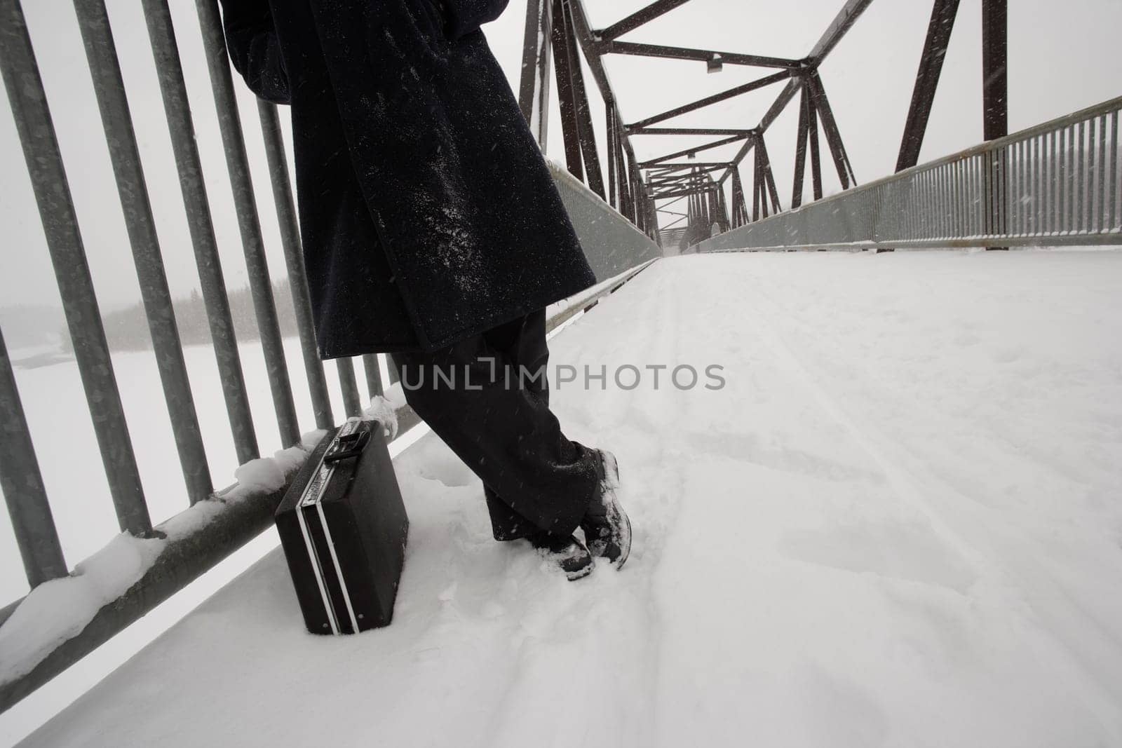 Man with briefcase waiting on snow covered bridge