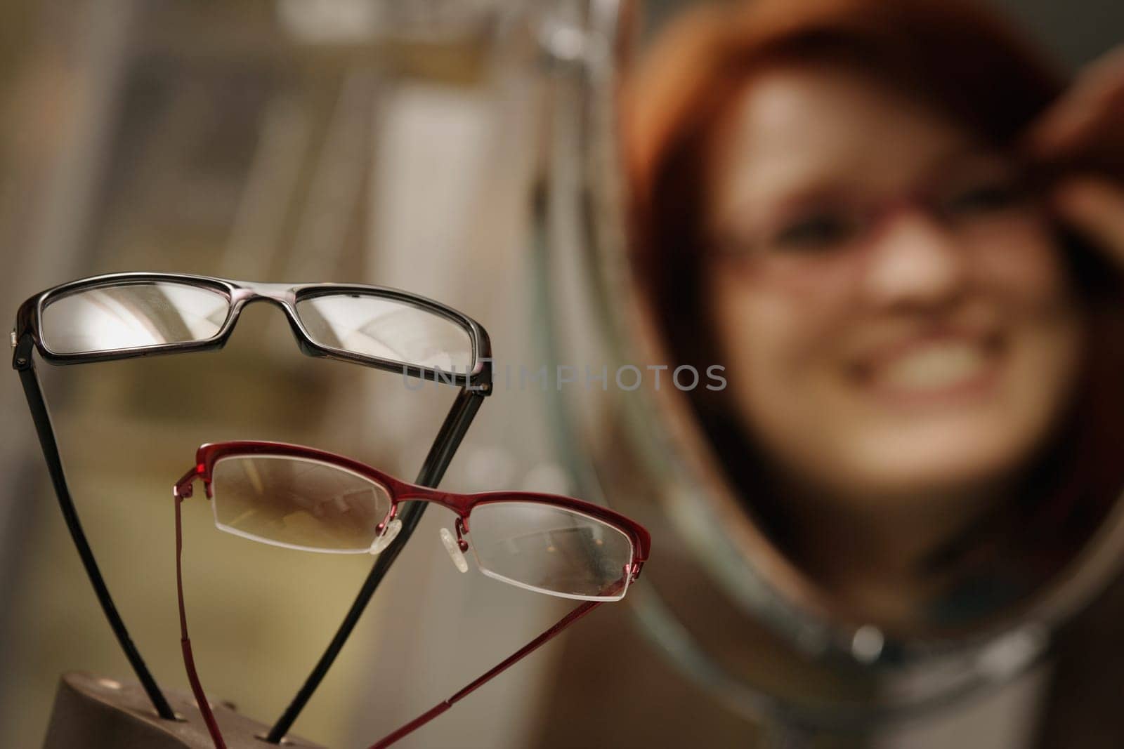 Optician's window display with woman trying on glasses in mirror in background