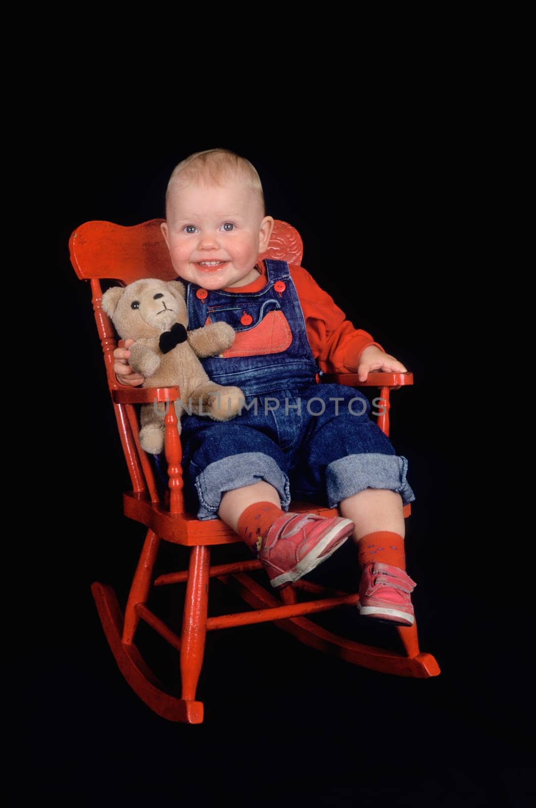 Toddler sitting in red rocking chair with teddy bear