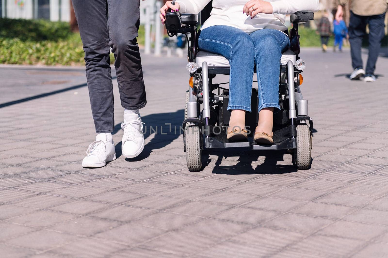 cropped photo of an unrecognizable woman using wheelchair with a man taking a walk by the city, concept of friendship and urban mobility for people with disability, copy space for text