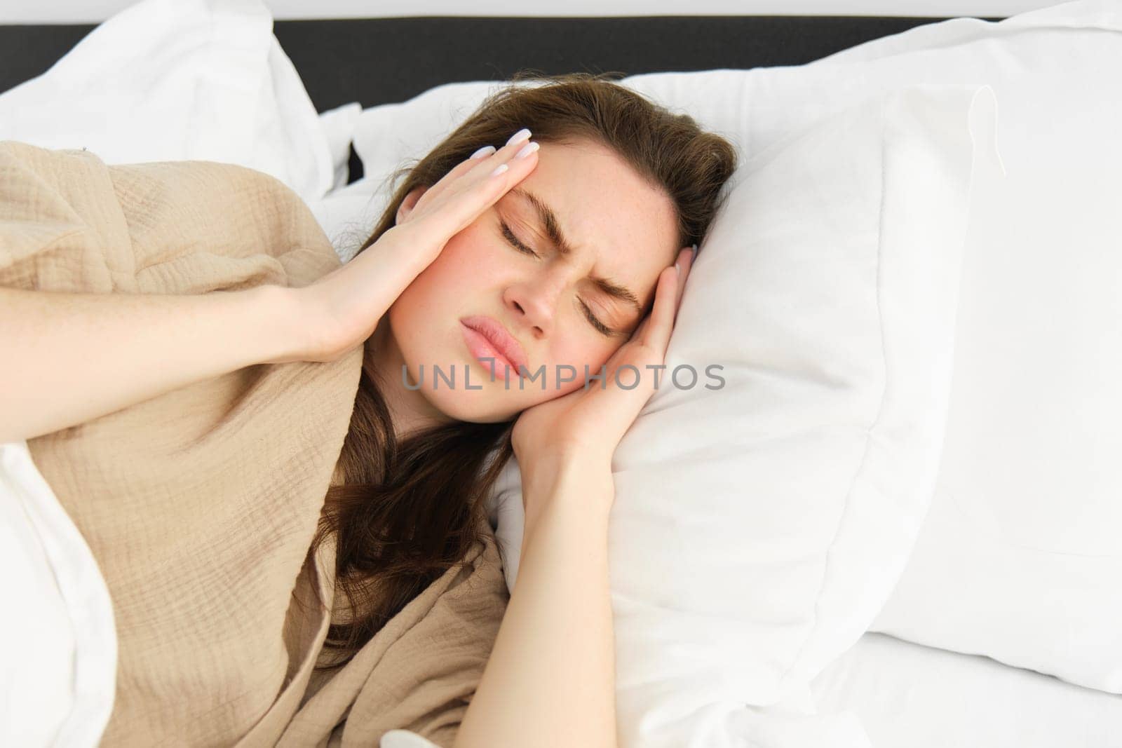 Portrait of woman lying in bed sick, touching headache from discomfort, has painful migraine, feel unwell, resting with eyes closed in pyjamas.