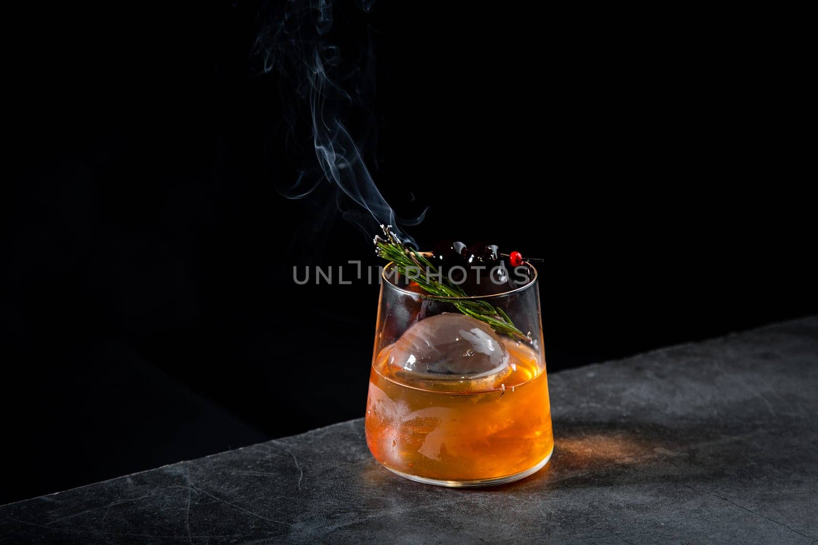 aromatic cocktail with a sprig of pine needles and round ice on a dark background, side view by tewolf