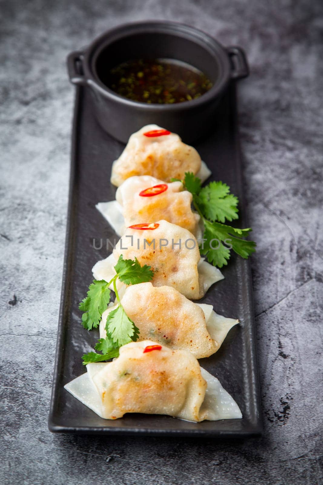 Asian dumplings with soy sauce, chili peppers and herbs on a dark background side view by tewolf