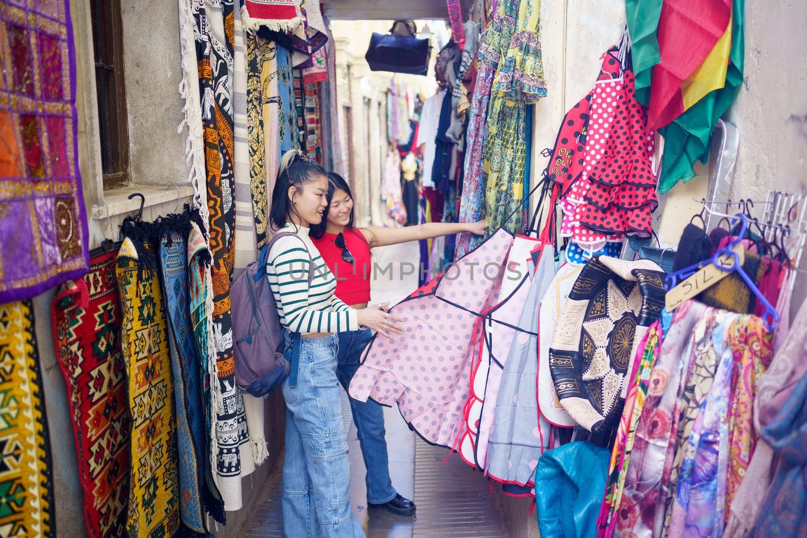 Two young Chinese women visiting Granada, Spain, looking at typical clothes in the typical handicraft stores in the Alcaicer a, old Muslim souk of Granada. Concept of Asian people traveling in Europe.