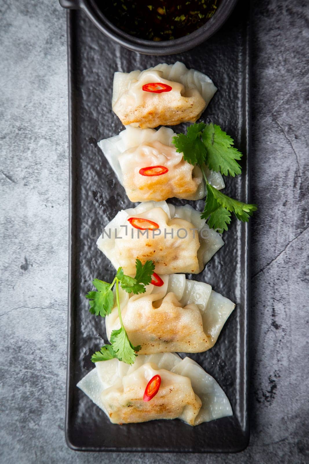 Asian dumplings with soy sauce, chili peppers and herbs on a dark background top view by tewolf