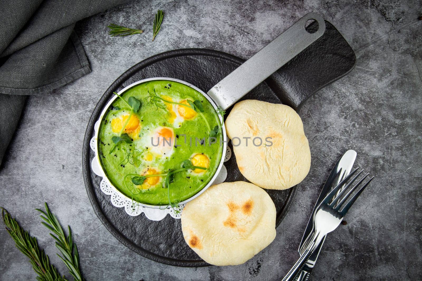 green broccoli soup with egg and herbs in a frying pan with flatbread, top view by tewolf