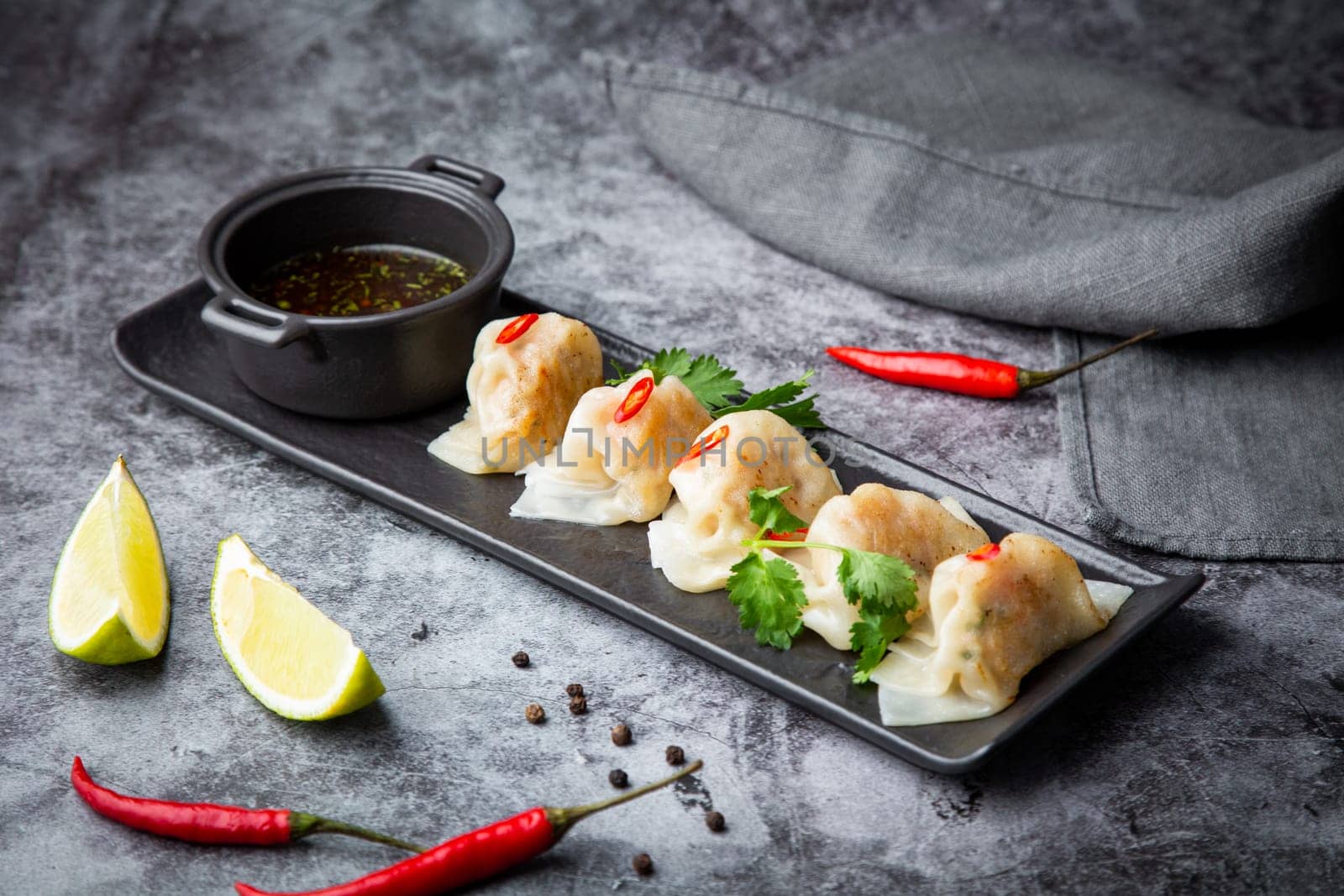 Asian dumplings with soy sauce, chili peppers and herbs on a dark background side view by tewolf