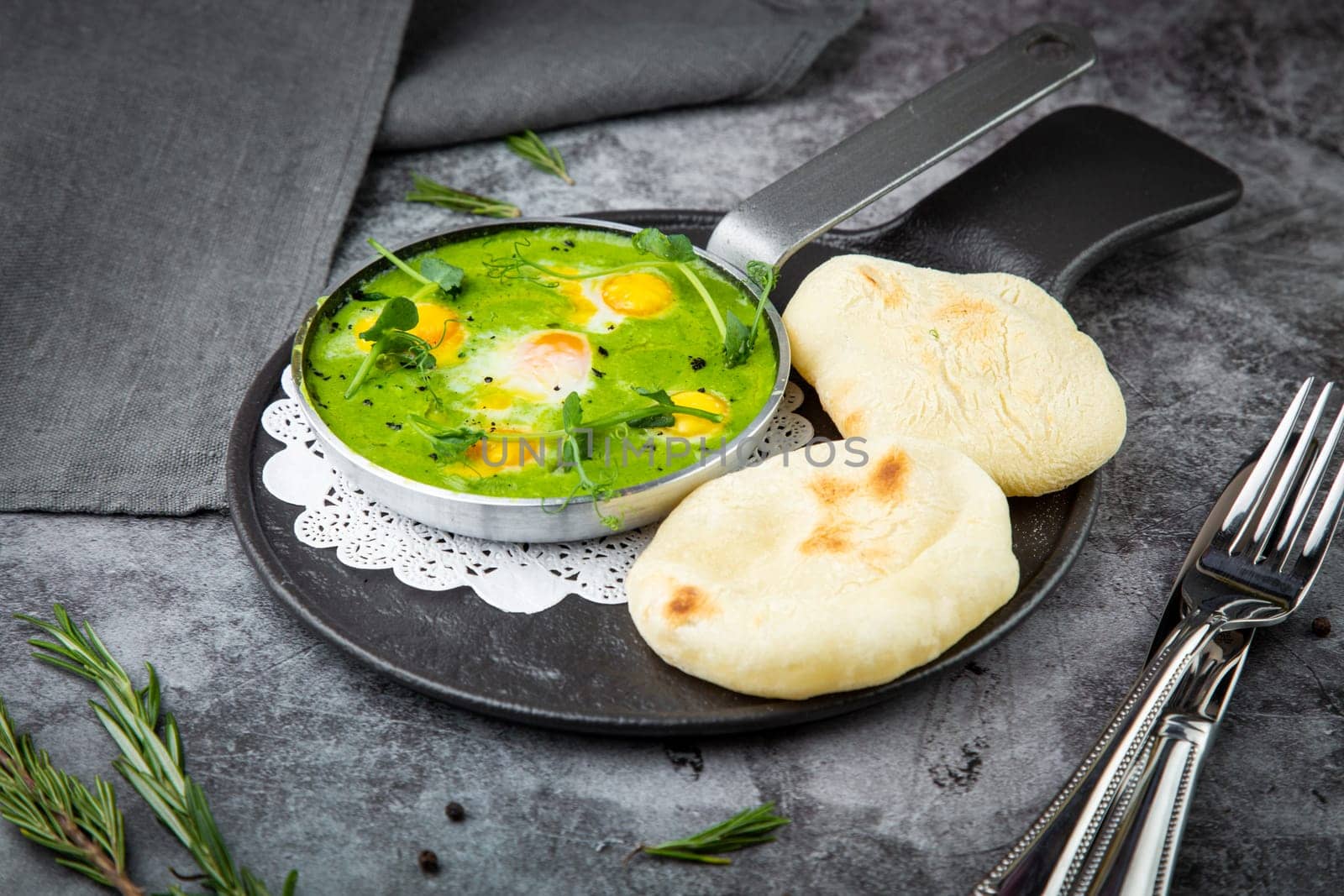 green broccoli soup with egg and herbs in a frying pan with flatbread, side view by tewolf