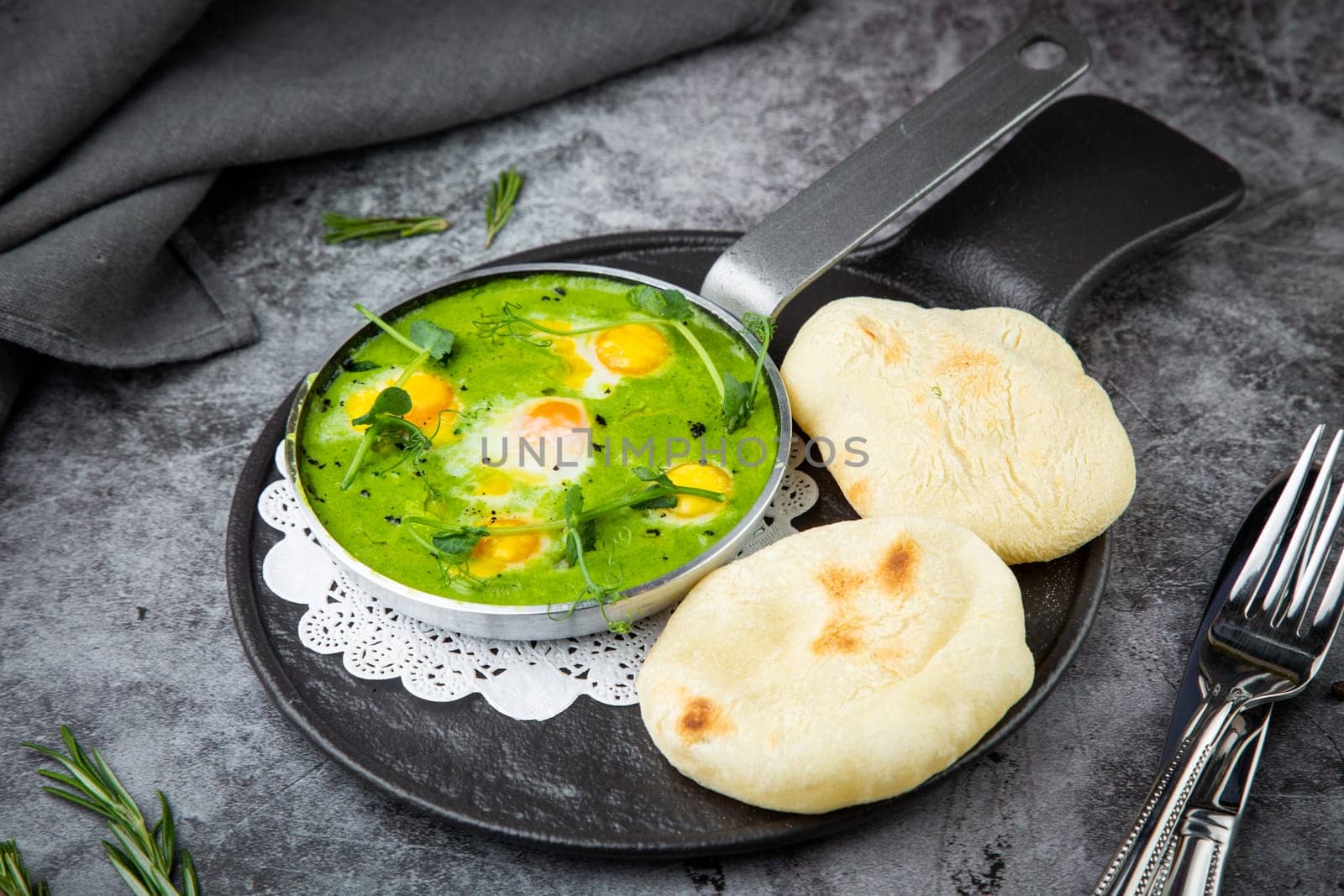 green broccoli soup with egg and herbs in a frying pan with flatbread, side view by tewolf