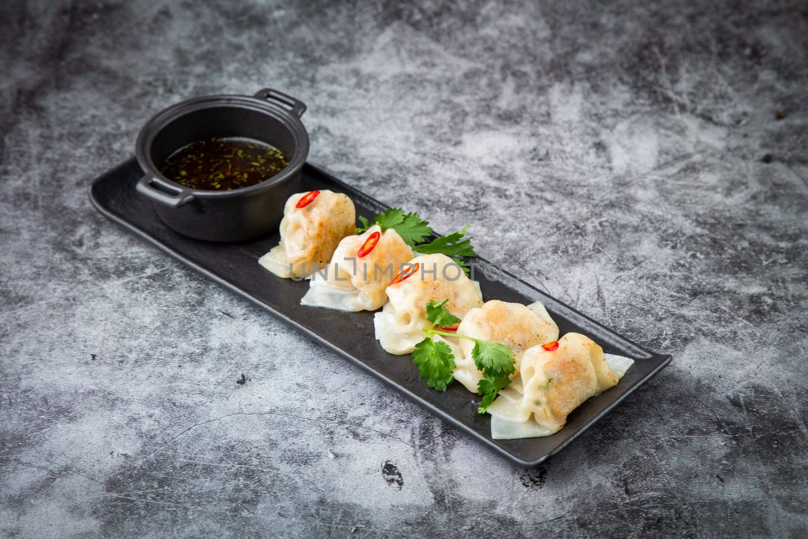 Asian dumplings with soy sauce, chili peppers and herbs on a dark background side view by tewolf