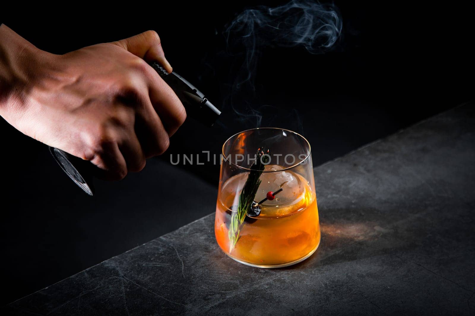 aromatic cocktail with a sprig of pine needles and round ice on a dark background, side view by tewolf