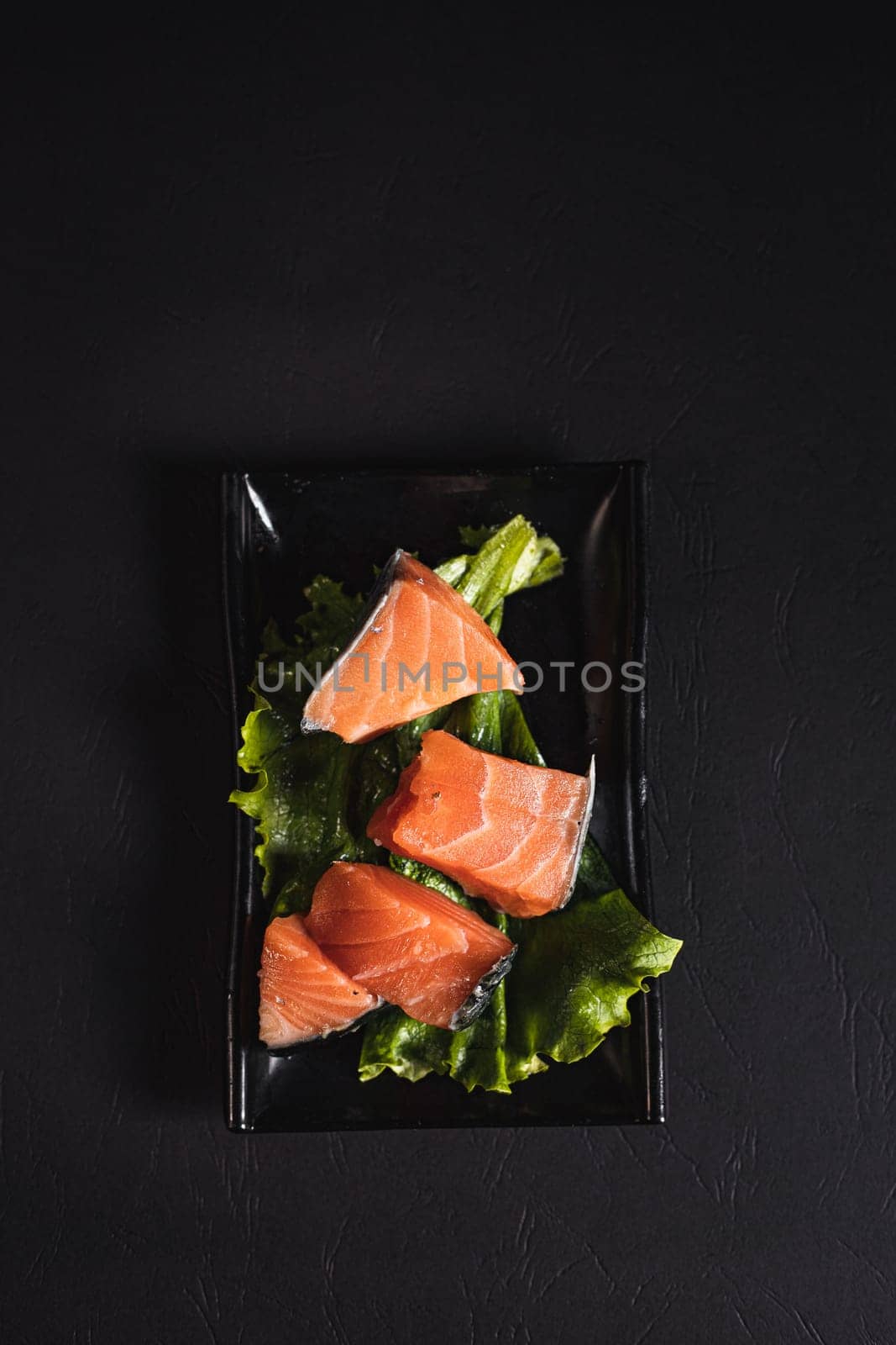 red fish on lettuce leaves on a black plate top view by tewolf