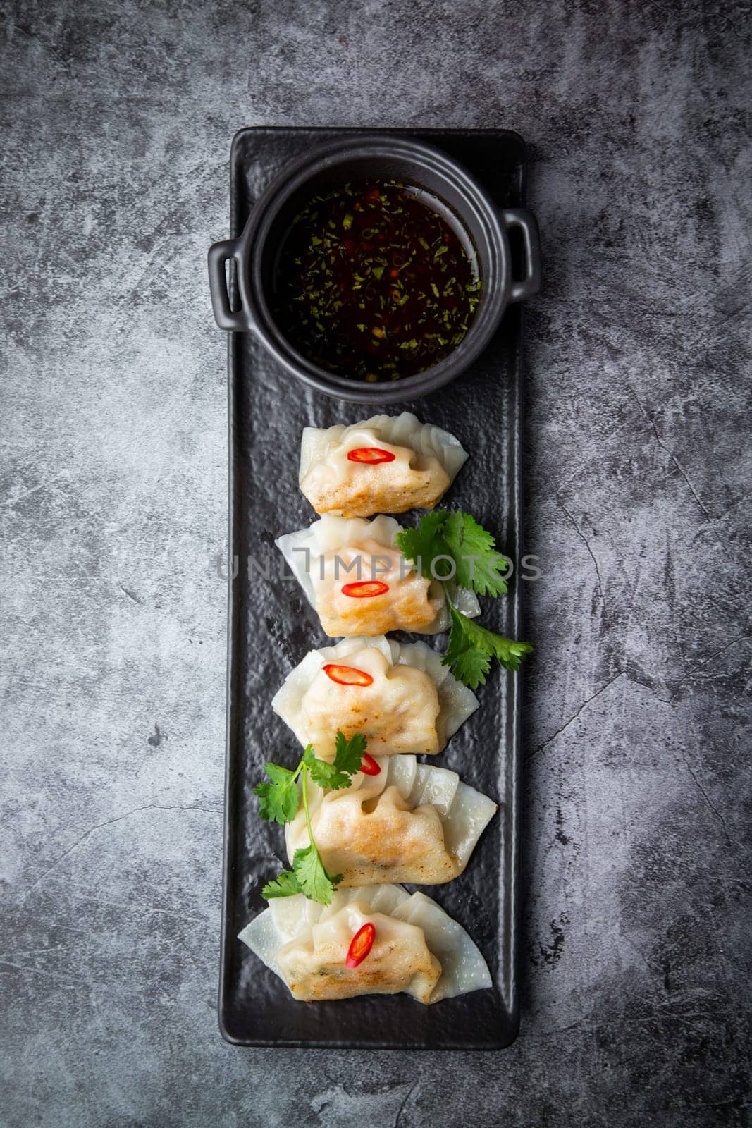 Asian dumplings with soy sauce, chili peppers and herbs on a dark background top view by tewolf