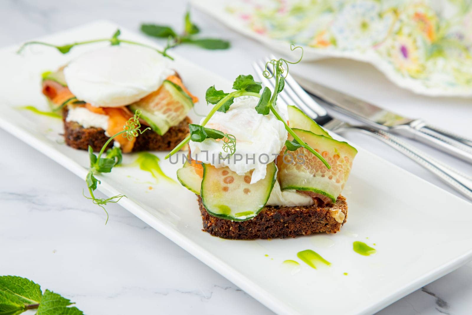 canapes on black bread with cheese, red fish, herbs and cucumber side view by tewolf