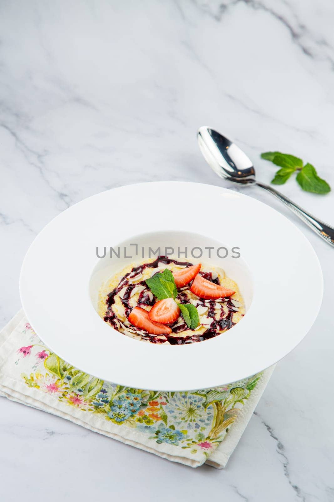 porridge with strawberries, mint and berry jam in a white plate