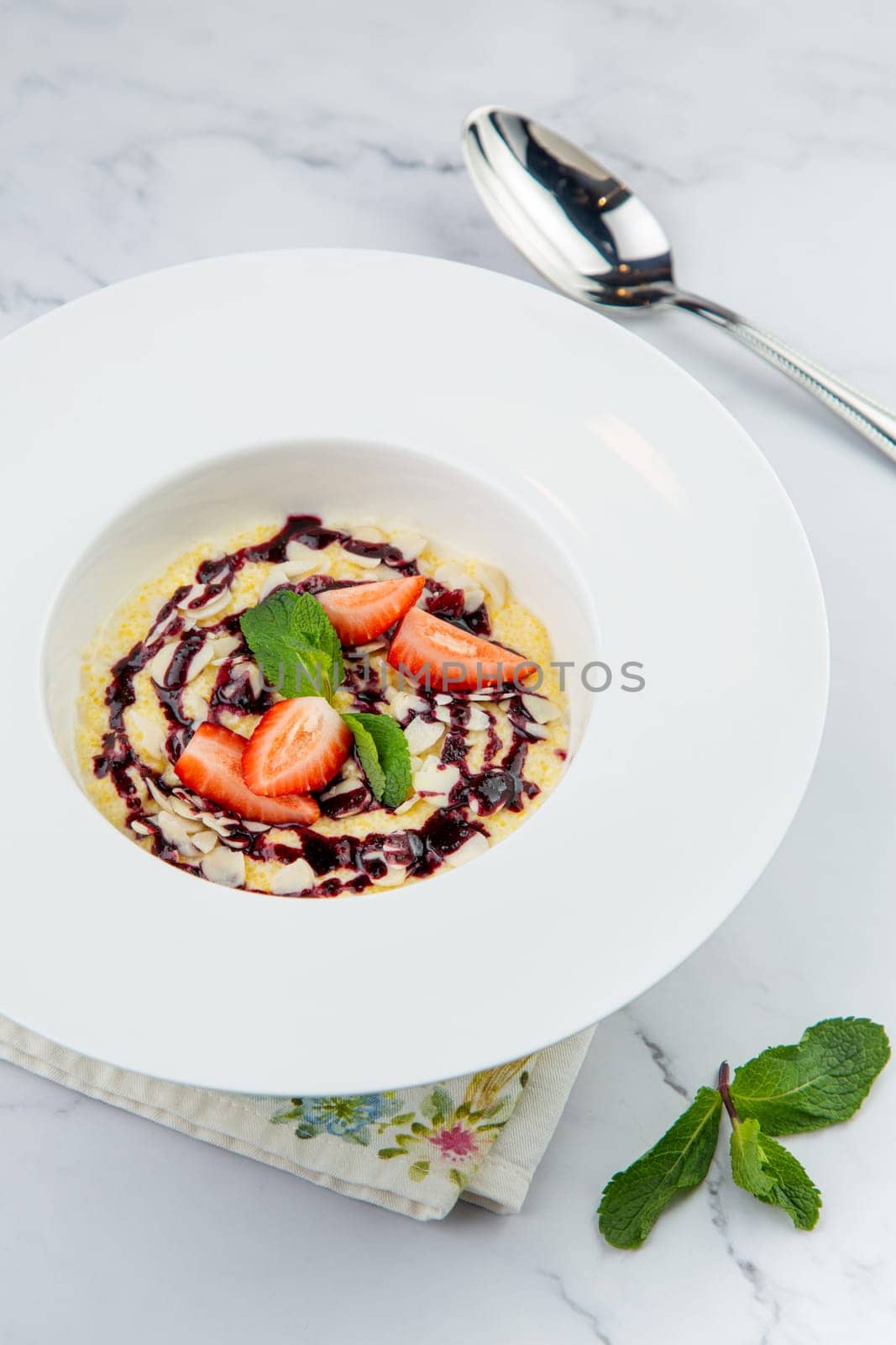 porridge with strawberries, mint and berry jam in a white plate