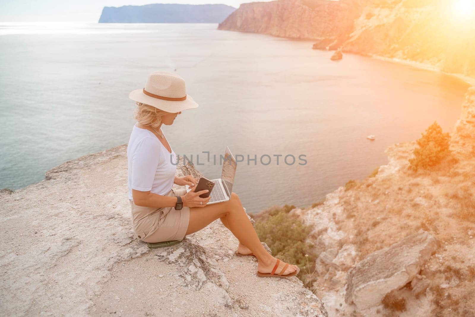 Freelance women sea working on the computer. Good looking middle aged woman typing on a laptop keyboard outdoors with a beautiful sea view. The concept of remote work