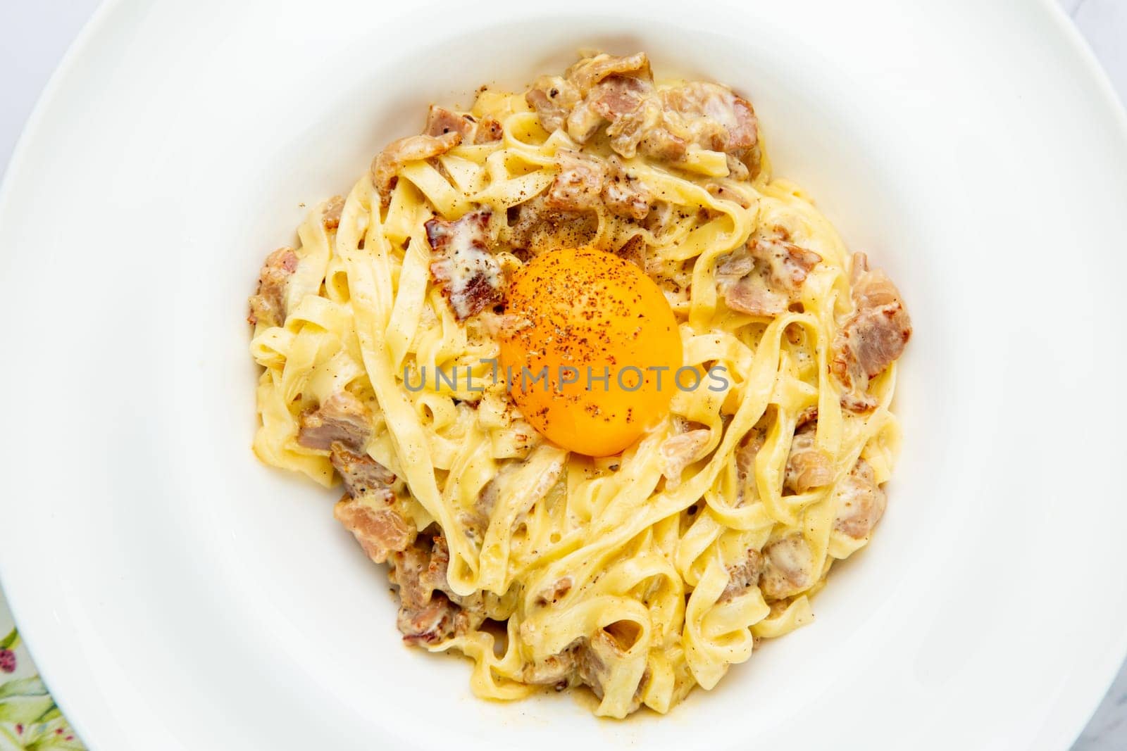 pasta in cream sauce with egg and black pepper on top view by tewolf