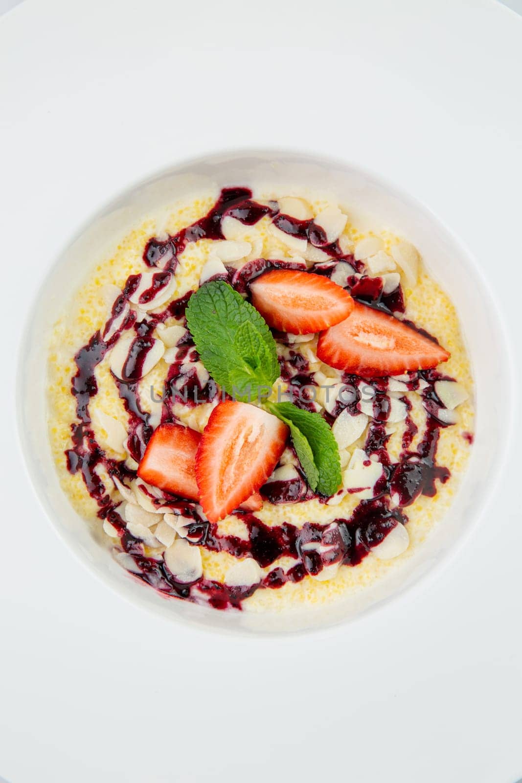 porridge with strawberries, mint and berry jam in a white plate, top view by tewolf