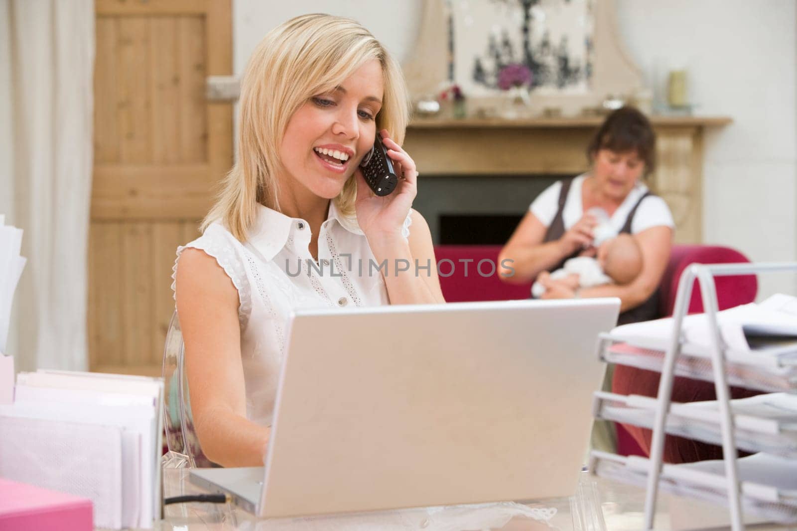 Woman in home office with laptop and telephone with mother and baby in backgroun