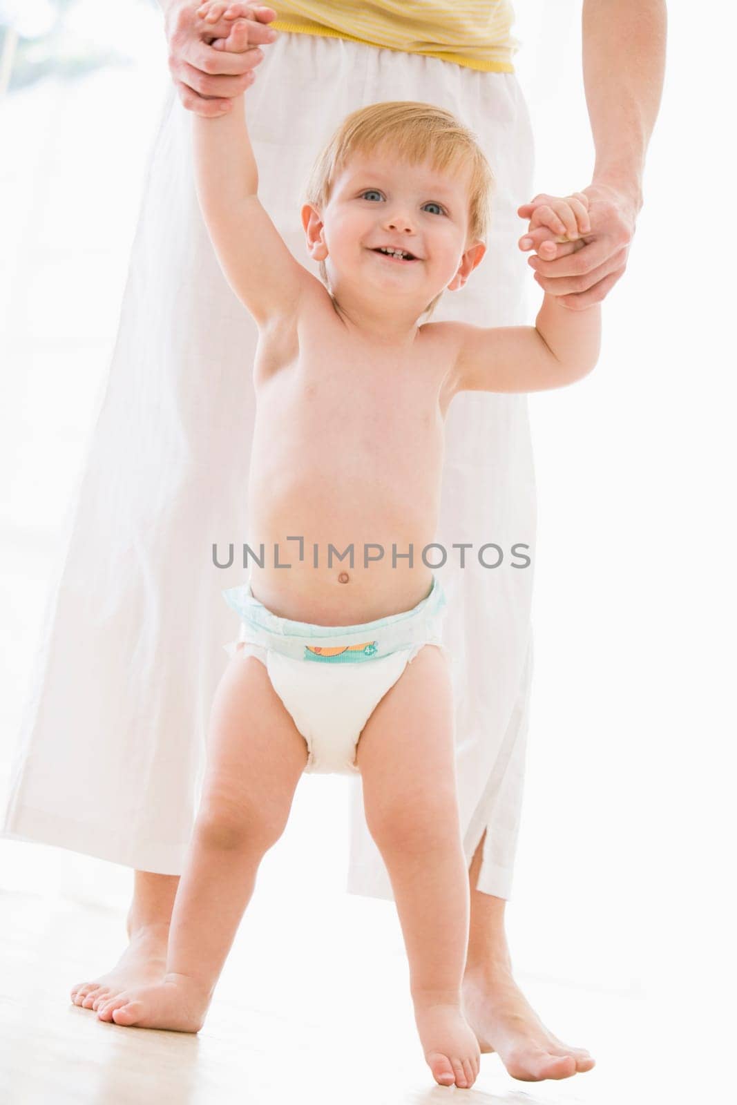 Mother helping baby walk indoors smiling