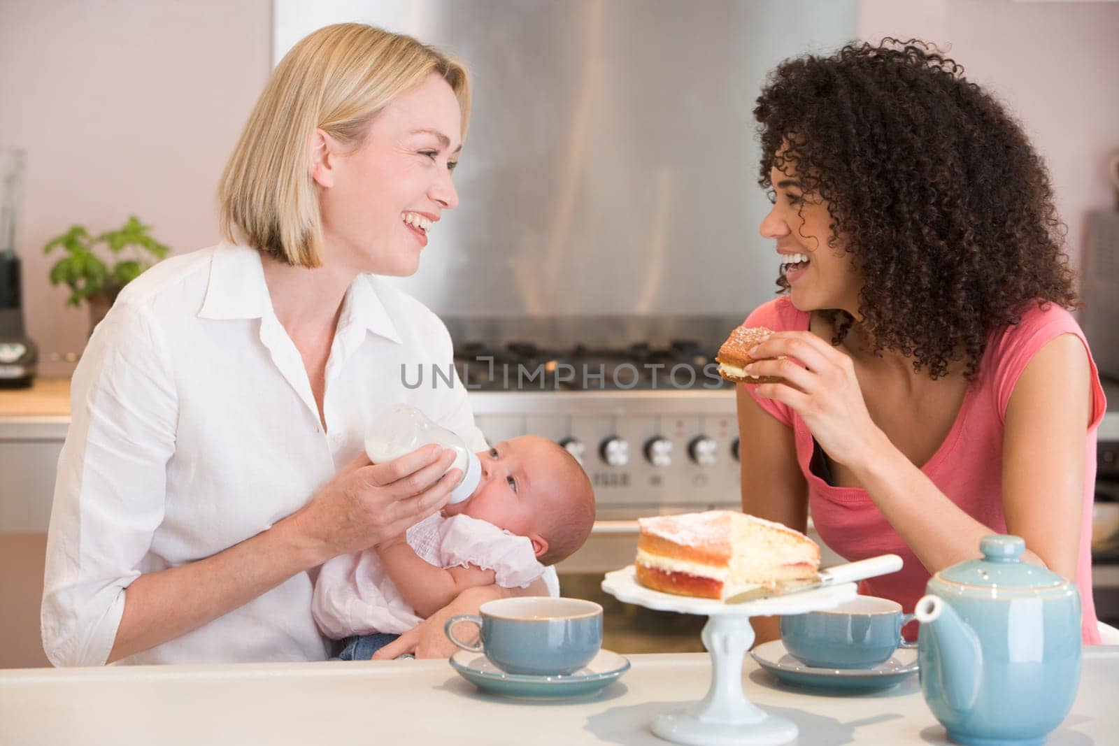 Mother and baby in kitchen with friend eating cake and smiling