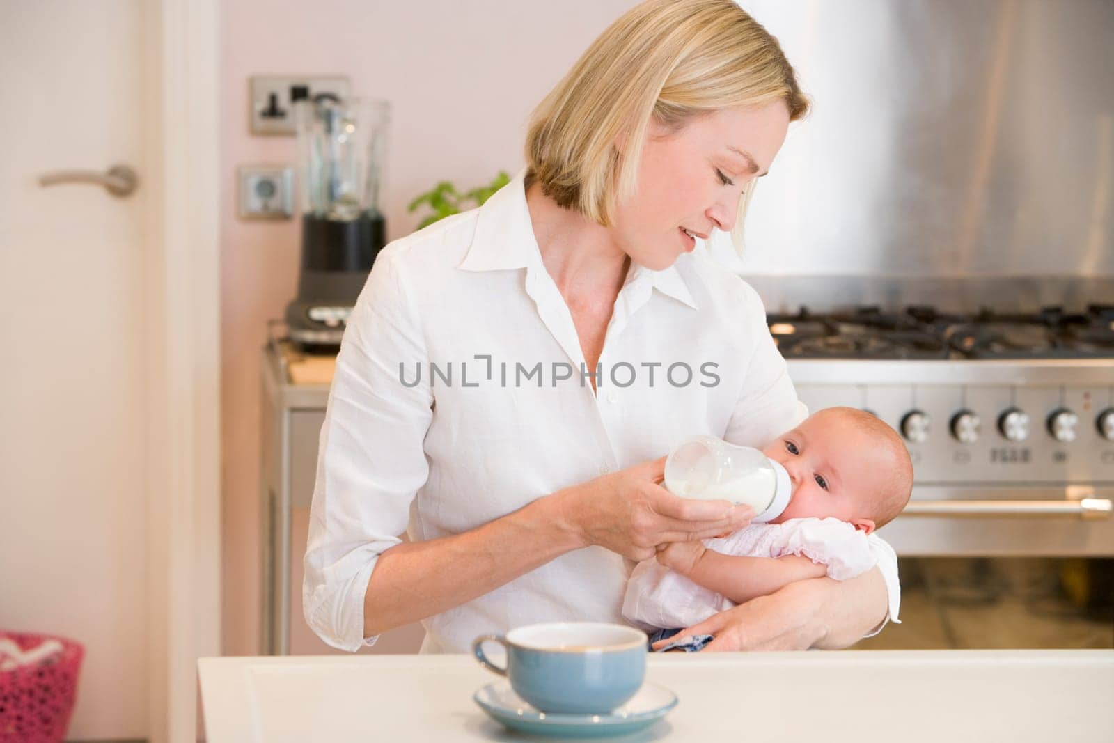 Mother feeding baby in kitchen with coffee