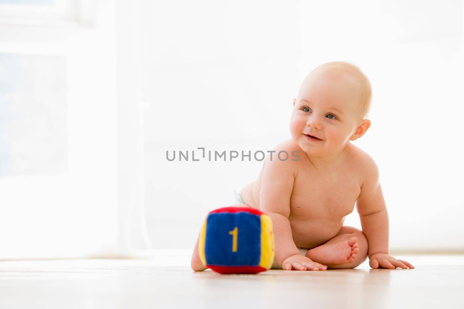 Baby sitting indoors with block smiling
