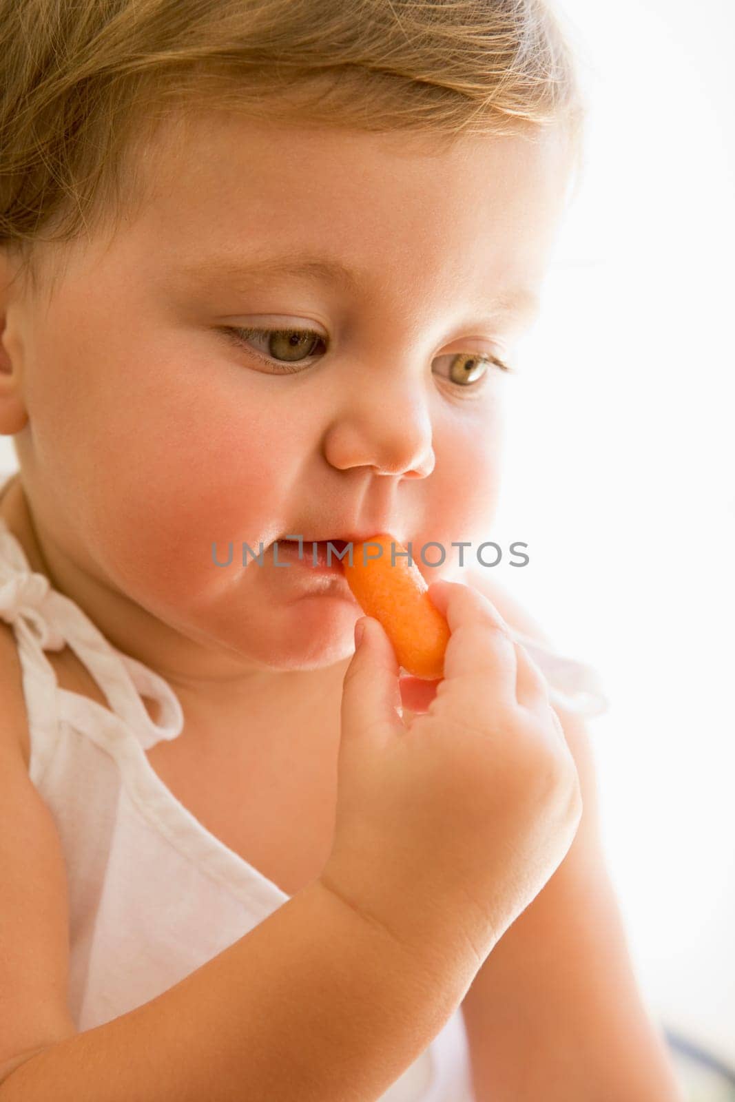 Baby indoors eating carrot.