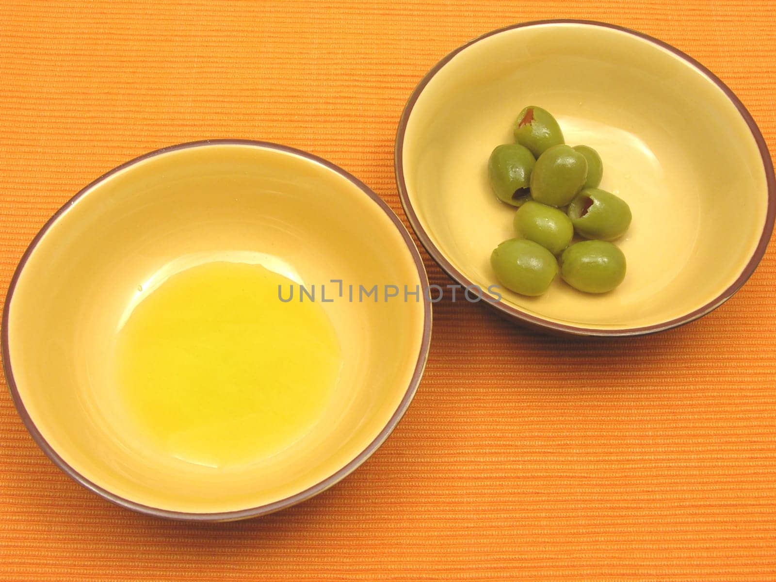 Two ceramic bowls with olive oil and olives on orange background