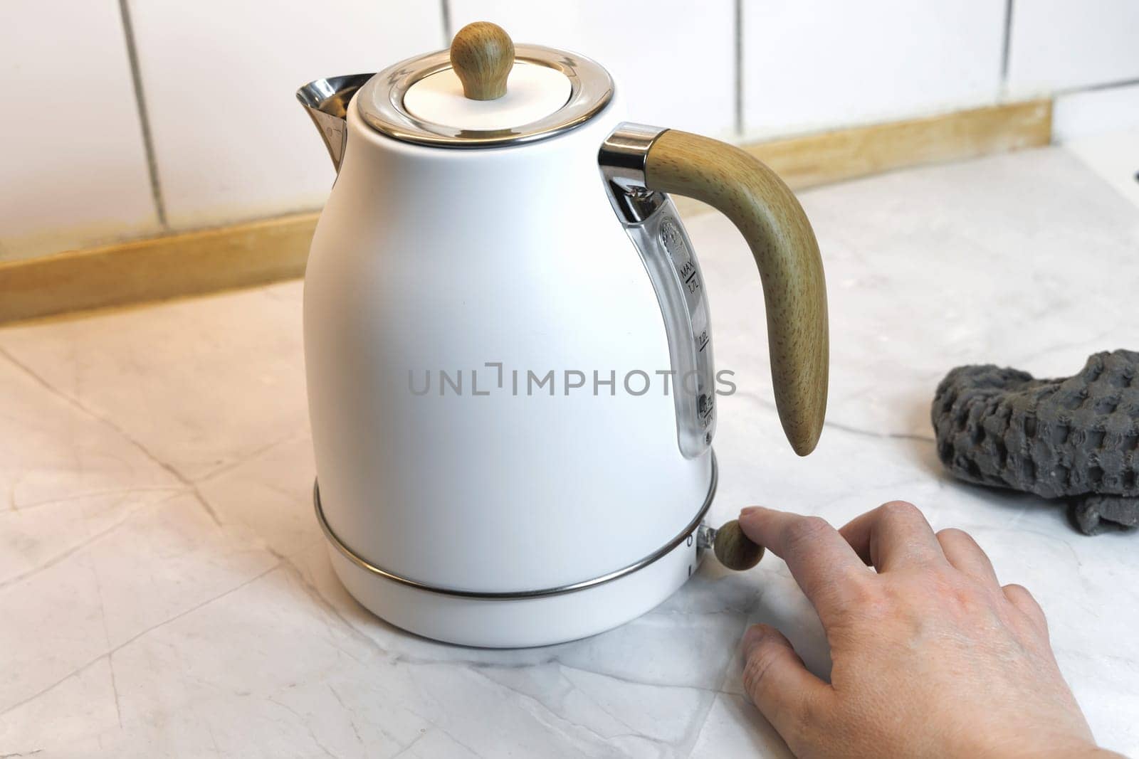 Female hand turns on white electric kettle. High quality photo