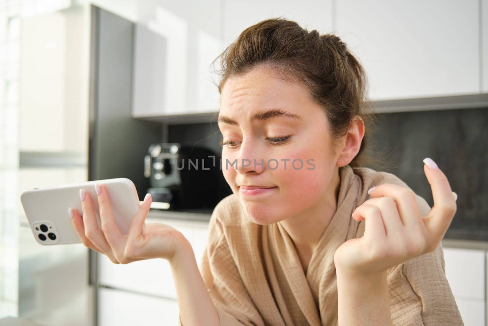 Attractive young cheerful girl baking at the kitchen, making dough, holding recipe book, having ideas by Benzoix