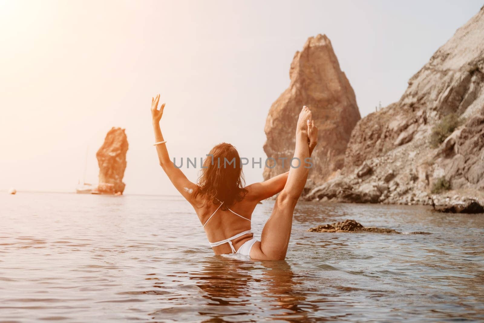 Young woman with black hair, fitness instructor in pink sports leggings and tops, doing pilates on yoga mat with magic pilates ring by the sea on the beach. Female fitness daily yoga concept