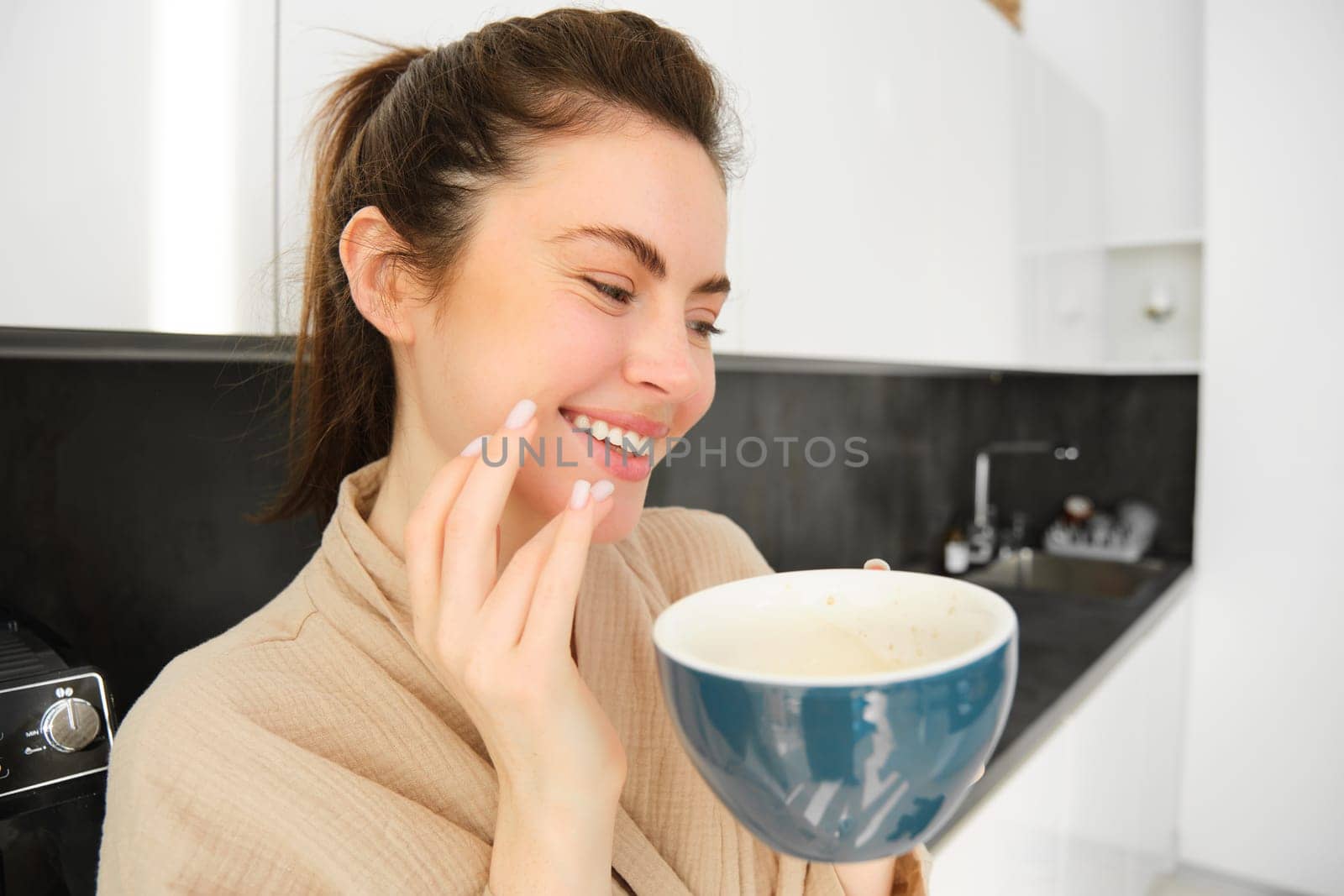Close up portrait of happy young woman drinking coffee in the kitchen, laughing and smiling.