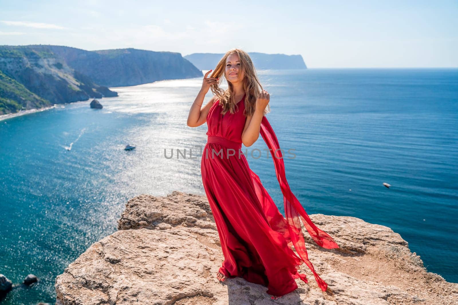 A woman in a red flying dress fluttering in the wind, against the backdrop of the sea