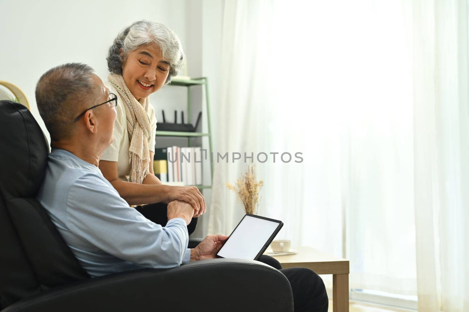 Image of happy retired couple resting on couch and using digital tablet searching for travel destination.