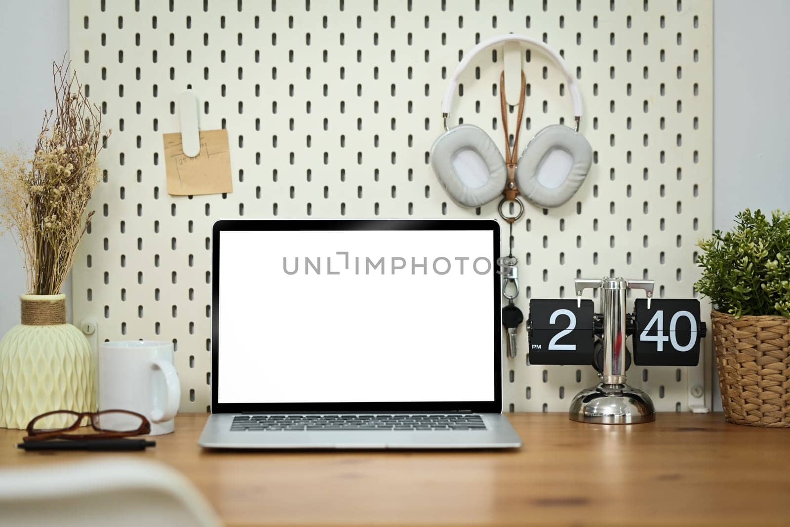 Front view of laptop, glasses, headphone, glasses and vintage flip clock on white table.