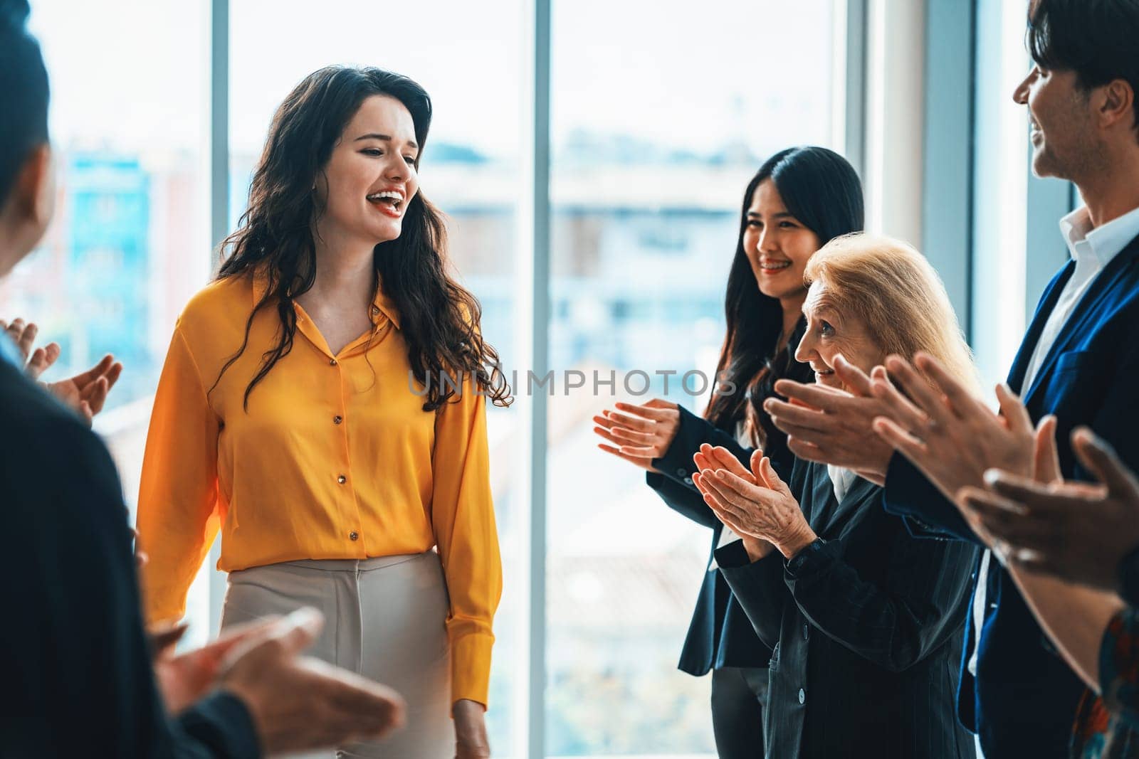 Successful businesswoman looking at camera with confidence while standing rounded with her coworker clapping hands. Diverse team celebrates promotion of new beautiful manager. Intellectual.