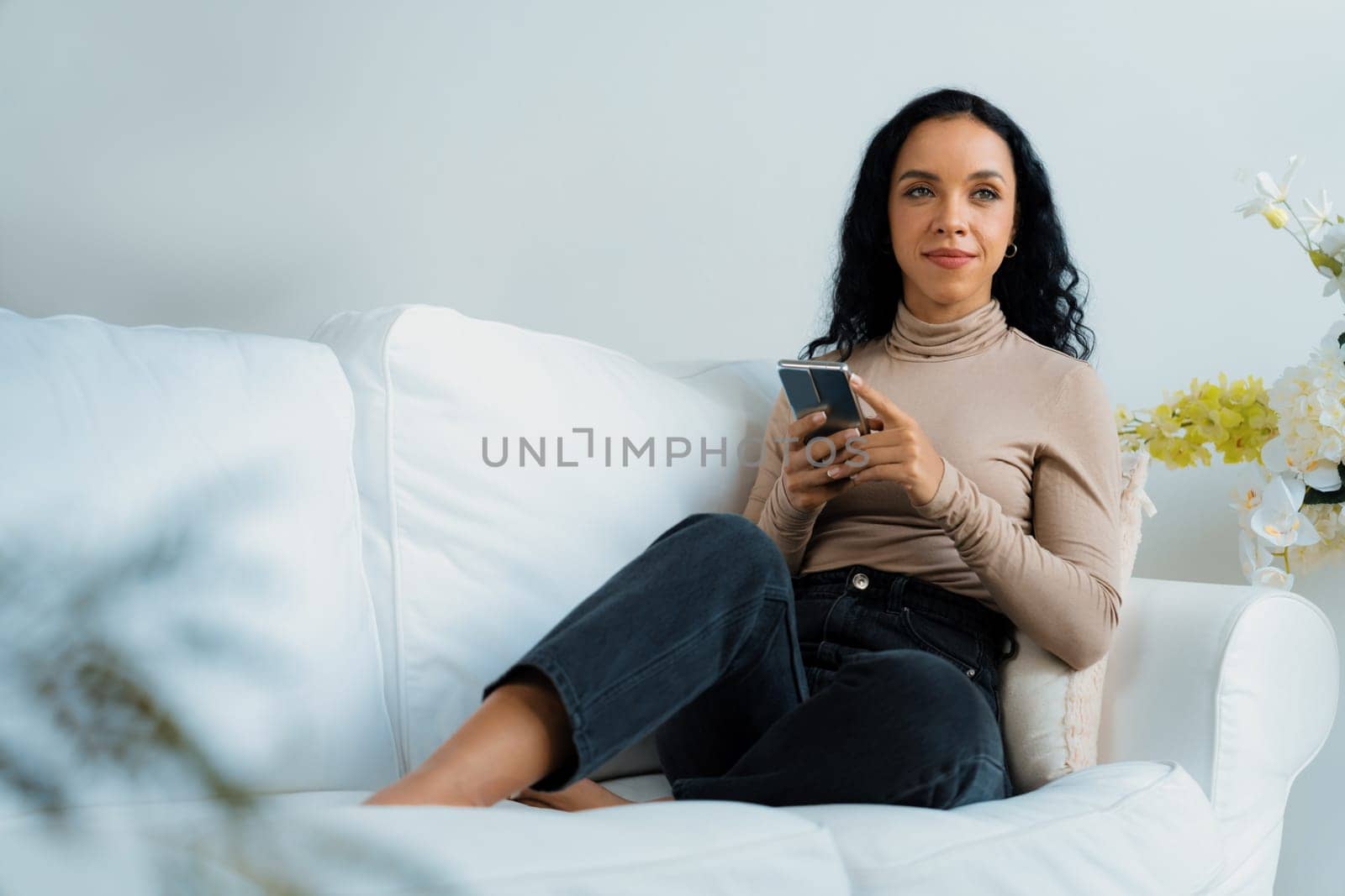 Relaxed young African American woman using crucial mobile phone on sofa couch by biancoblue