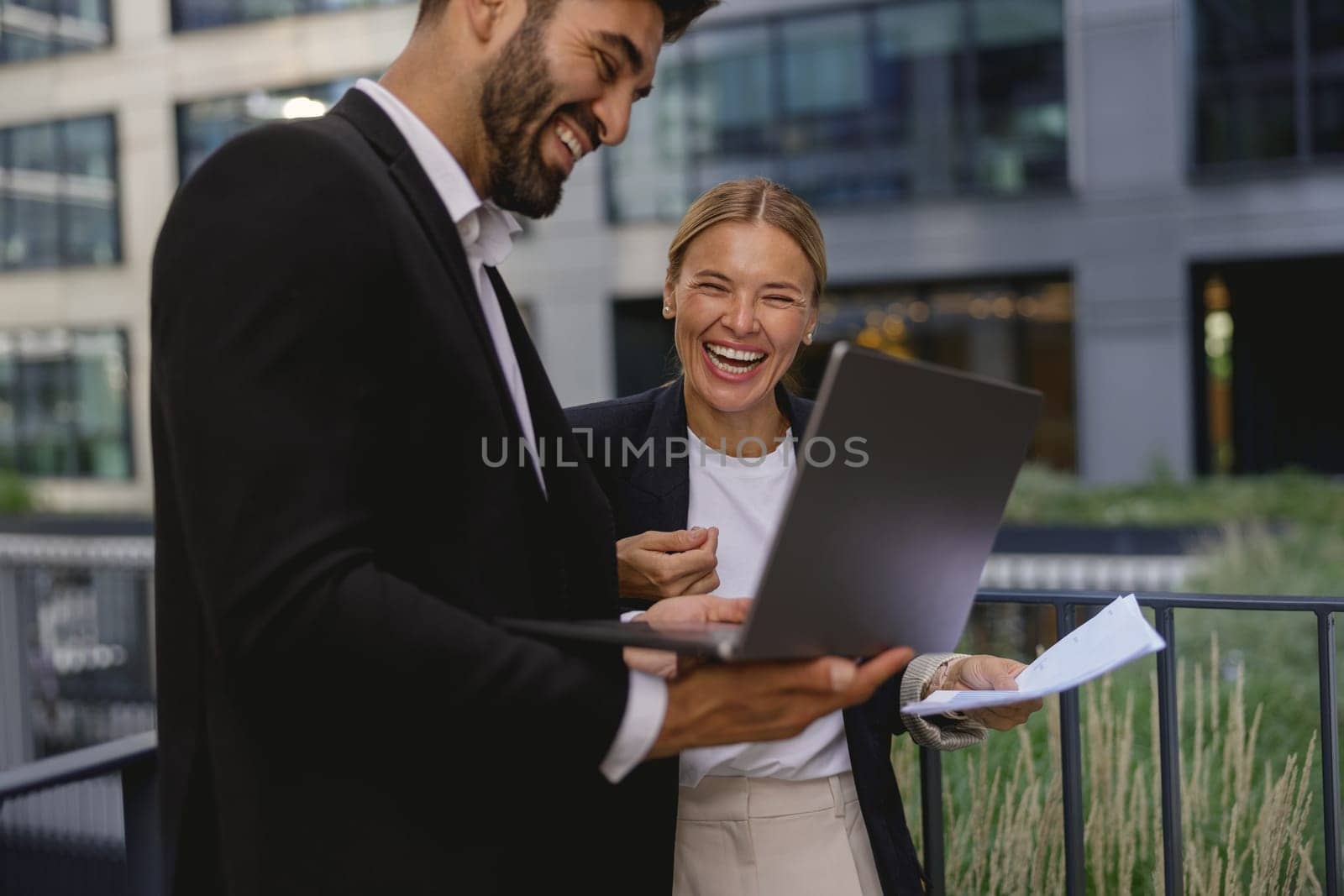 Smiling business colleagues discuss biz issue while use laptop standing on office terrace by Yaroslav_astakhov