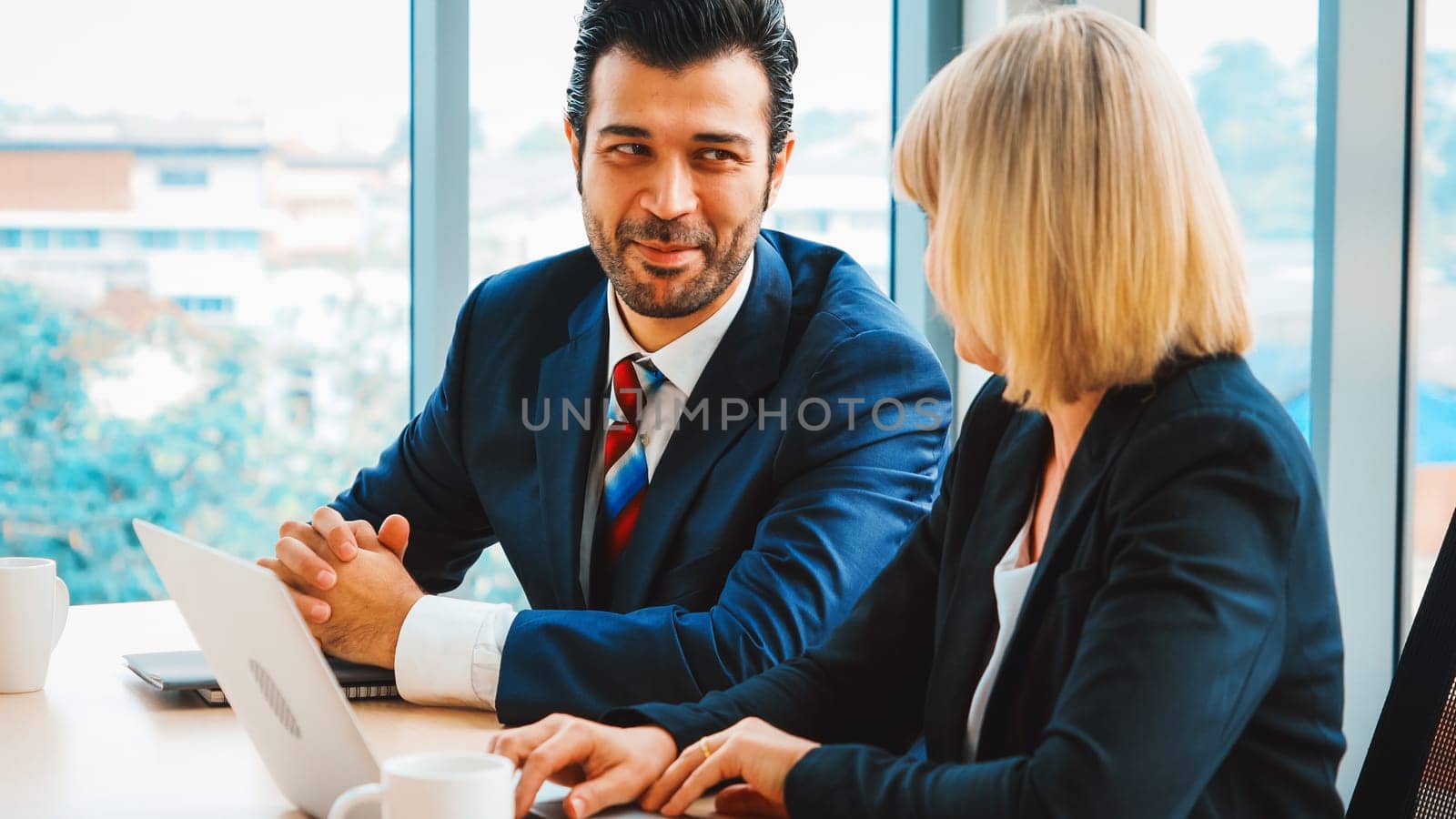 Two business people talk project strategy at office meeting room. Businessman discuss project planning with colleague at modern workplace while having conversation and advice on financial report. Jivy