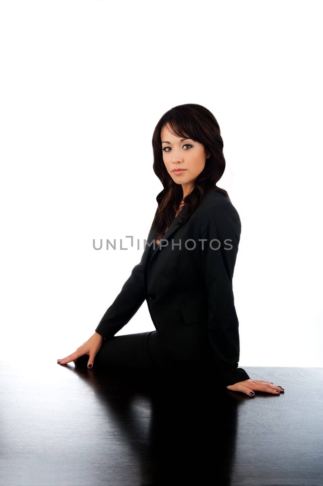Serious, young, attractive businesswoman sitting on desk on whit