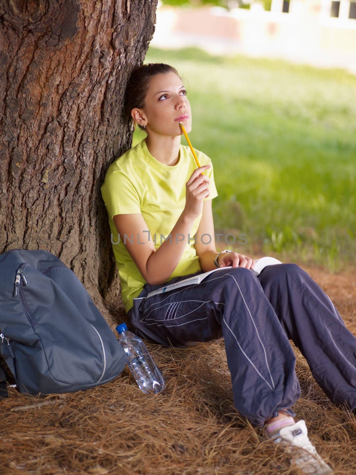 young woman studying outdoors and leaning on tree