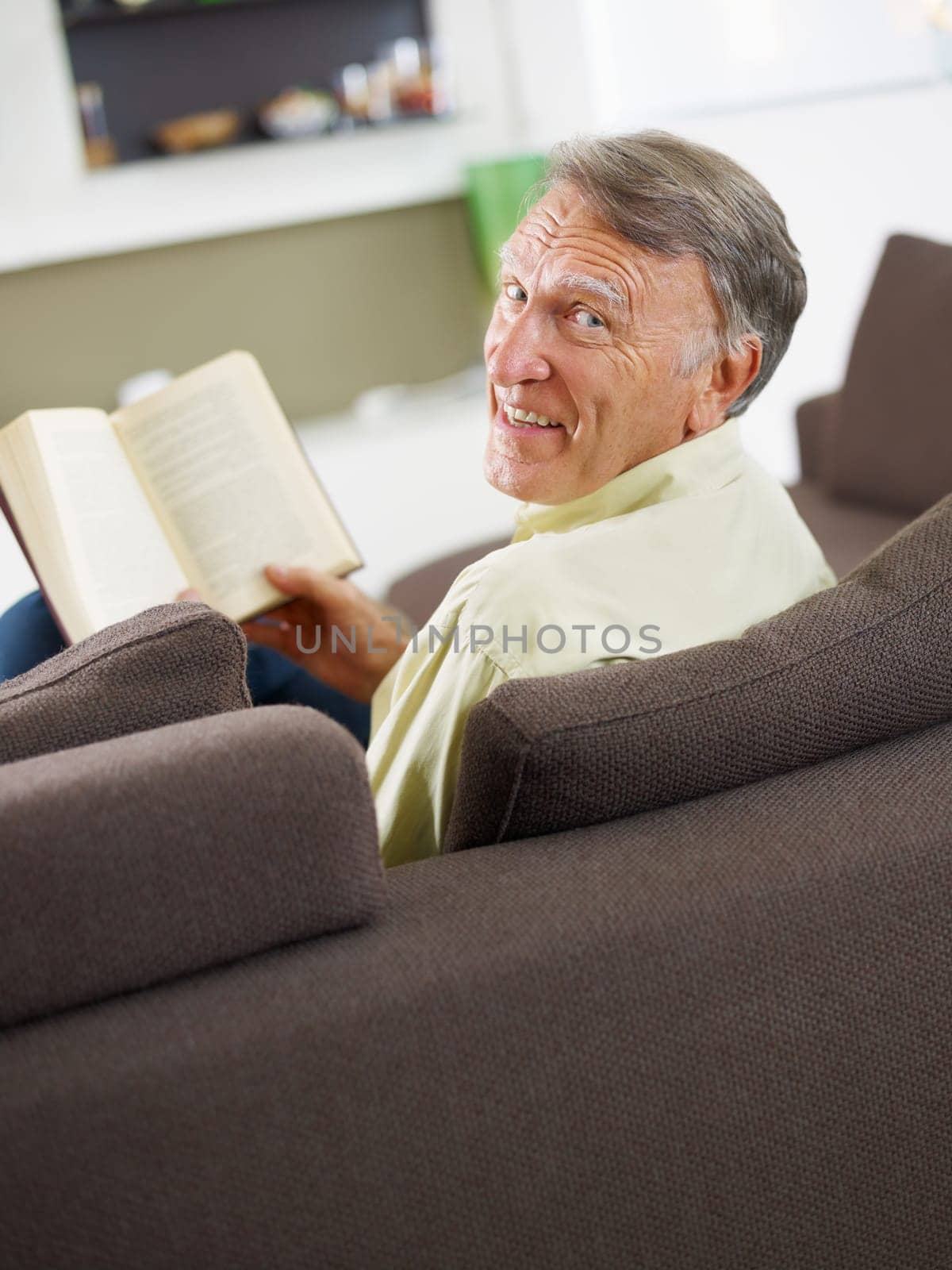 senior man reading book at home and looking over shoulders