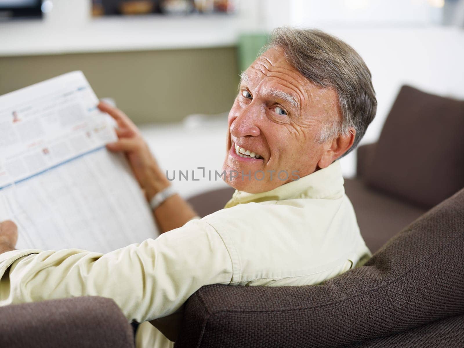 senior man reading newspaper at home and looking over shoulders