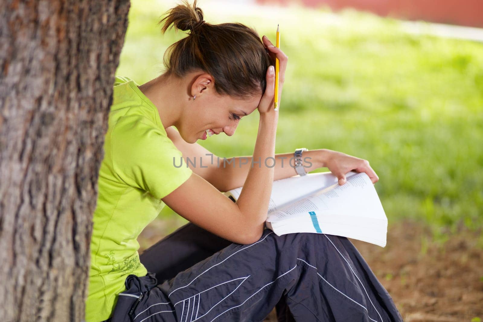 young woman studying outdoors and leaning on tree
