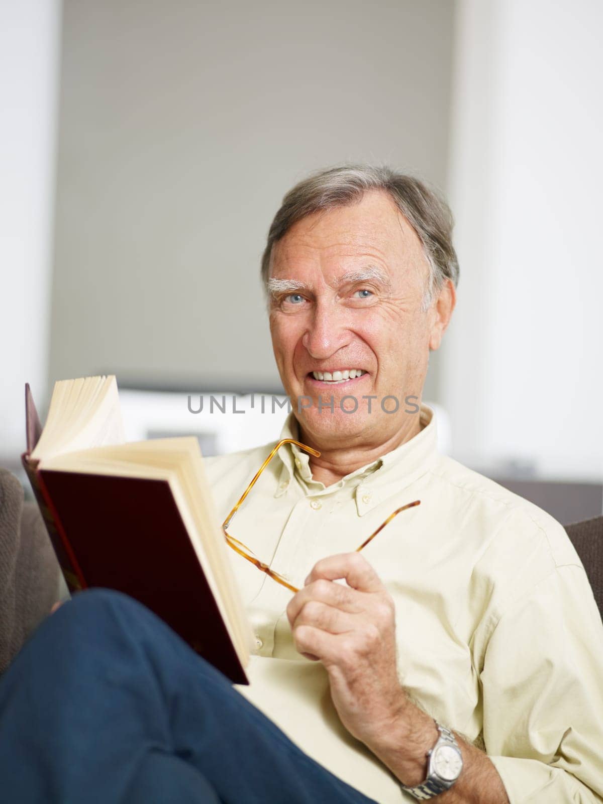 senior man reading book at home and looking at camera. Copy space