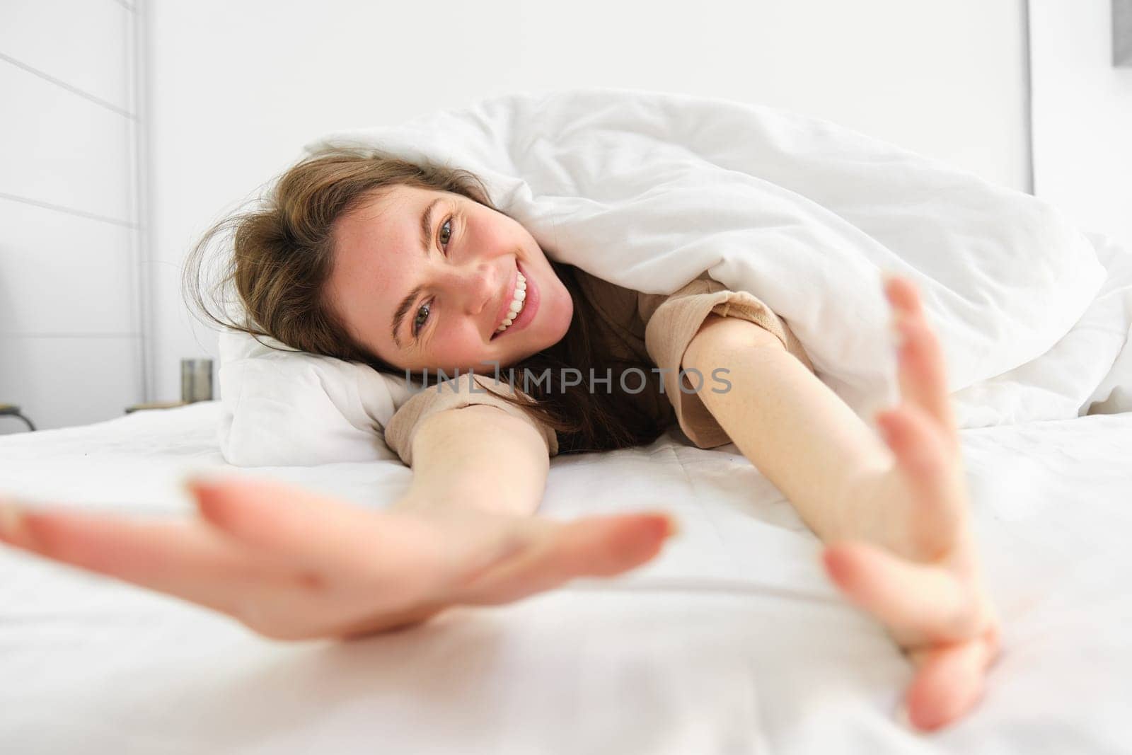 Cheerful girl stretching her arms in bed, waking up from good sleep or nap, enjoying the morning by Benzoix